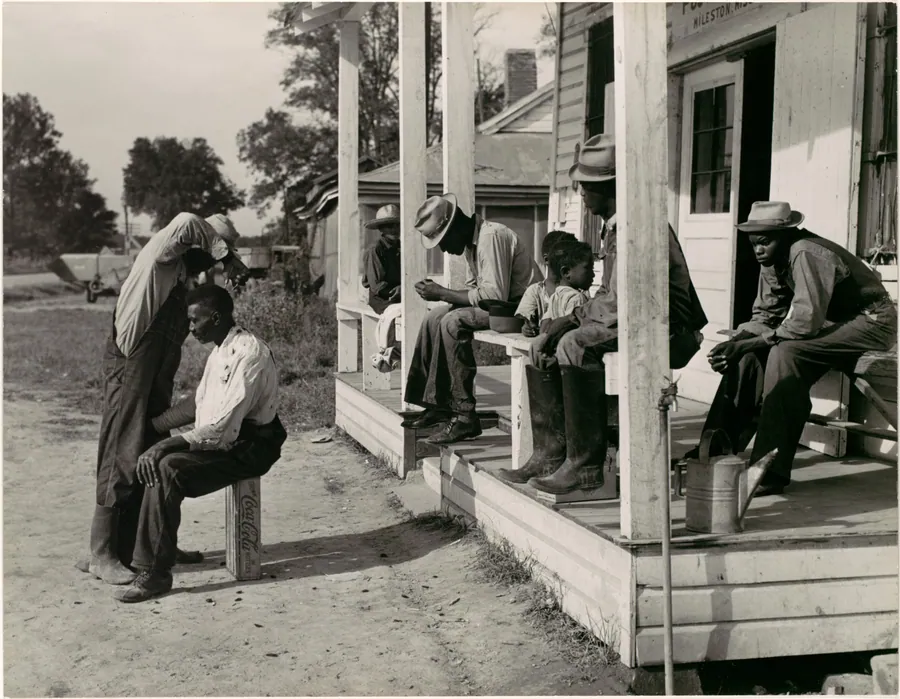 [Haircutting in Front of General Store and Post Office on Marcella Plantation, Mileston, Mississippi] by Marion Post Wolcott