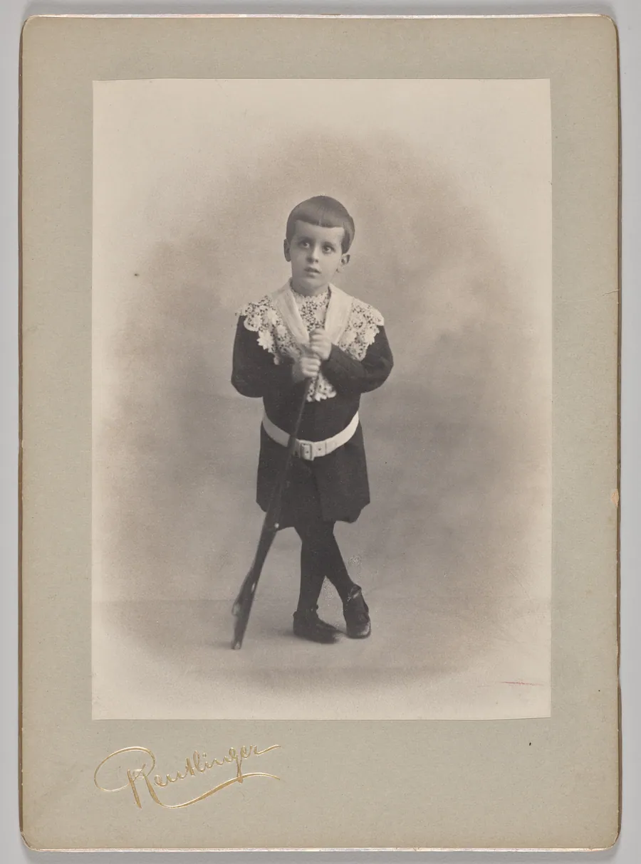 Untitled (young boy with lace collar and toy rifle) by Reutlinger Studios
